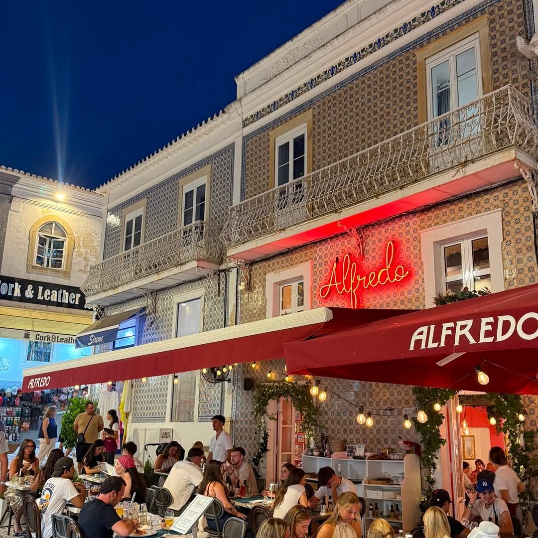 Fachada de azulejos do Alfredo ao anoitecer, com letreiro de néon vermelho, toldo vermelho e as mesas da esplanada cheias